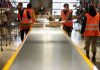 Workers in warehouse sorting packages on conveyor.