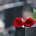 Two red roses on a black tombstone.