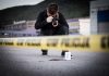 Person photographing crime scene evidence behind police tape