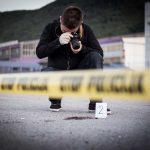 Person photographing crime scene evidence behind police tape