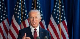 Man speaking at podium with American flags behind