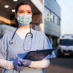 Doctor wearing mask and gloves holding clipboard outside hospital