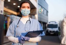 Doctor wearing mask and gloves holding clipboard outside hospital
