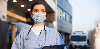 Doctor wearing mask and gloves holding clipboard outside hospital