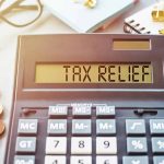 Calculator display reads TAX RELIEF amidst coins and glasses