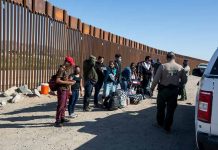 Group of people at border wall with patrol agents