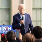 Man speaking at an outdoor event with Biden sign