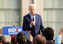 Man speaking at an outdoor event with Biden sign