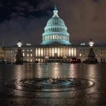 U.S. Capitol building illuminated at night with wet pavement.
