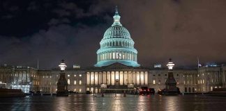 U.S. Capitol building illuminated at night with wet pavement.