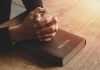 Hands praying on a Bible