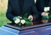 People placing white roses on a casket