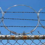 Barbed wire and metal fencing against blue sky