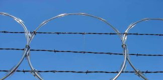 Barbed wire and metal fencing against blue sky