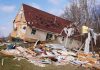 A severely damaged house tilted on its side surrounded by debris
