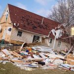 A severely damaged house tilted on its side surrounded by debris