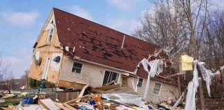 A severely damaged house tilted on its side surrounded by debris