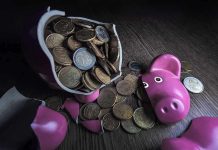 A broken pink piggy bank with coins spilling out onto a wooden surface