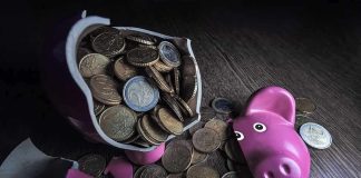 A broken pink piggy bank with coins spilling out onto a wooden surface