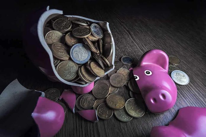 shutterstock_147048368.jpg A broken pink piggy bank with coins spilling out onto a wooden surface