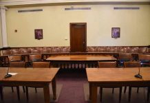 Empty courtroom with wooden tables, chairs, and a door.