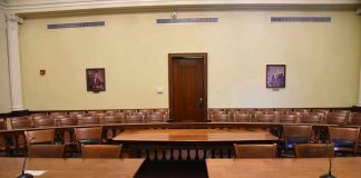 Empty courtroom with wooden tables, chairs, and a door.