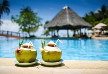Two coconut drinks with straws beside a swimming pool