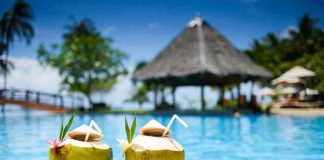 Two coconut drinks with straws beside a swimming pool