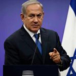Man in suit giving speech in front of Israeli flag.