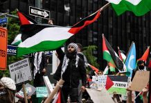 Protesters with flags and signs, one holding a megaphone.