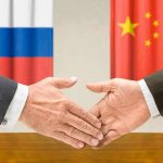 Two hands shaking in front of Russian and Chinese flags