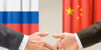 Two hands shaking in front of Russian and Chinese flags