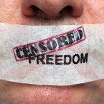 Close-up of a persons mouth covered with tape that reads CENSORED FREEDOM