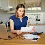 Woman shocked reading a document at home.