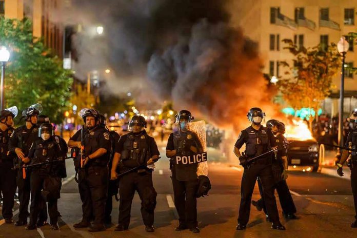 1796220283 Police officers in riot gear near burning car.