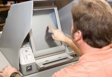 Person using touchscreen voting machine in polling booth.