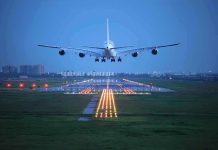 An airplane approaching the runway at night with landing lights illuminated